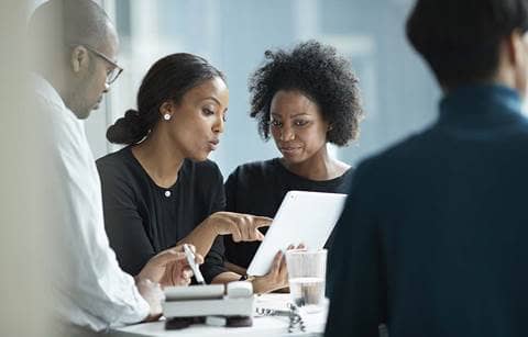 Three business professionals referring to a report on their tablet computer.