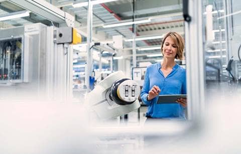 Factory worker inspecting robotic machine/arm in the factory floor.