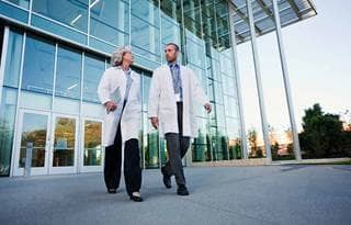 Two doctors walking together outside of a modern hospital.